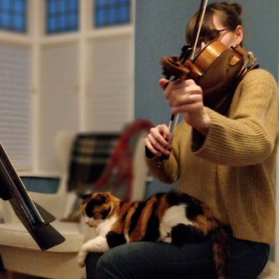 A photo of Robyn tuning her viola whilst her tabby cat, Sophie is sitting on her lap.